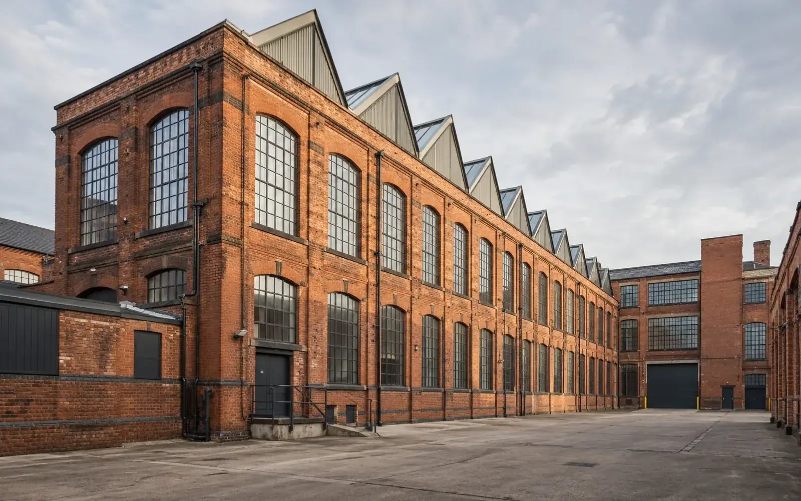 Red brick commercial mill building with repeated windows and a sawtooth roof